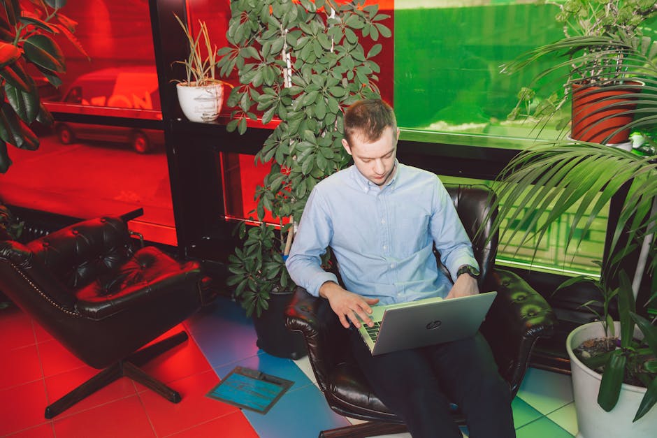 Young man using laptop in a vibrant, plant-filled modern office environment for remote work.