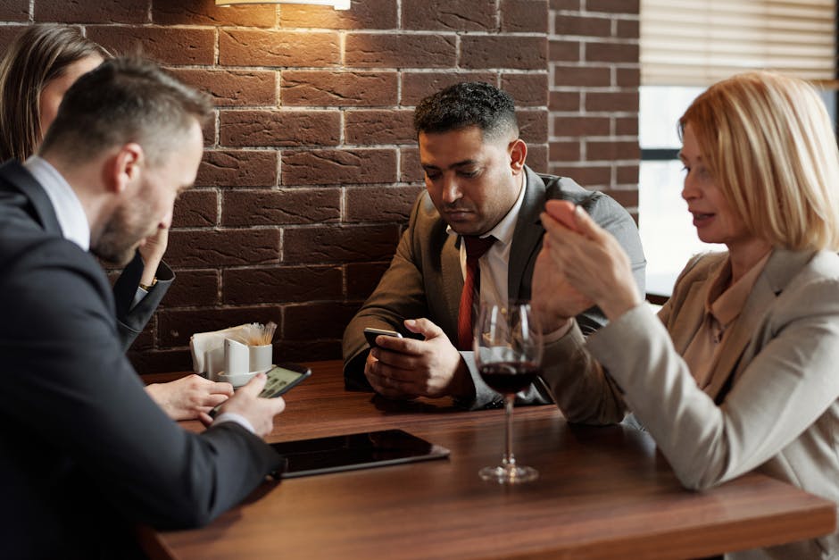 Diverse business team having a discussion at a café, enjoying wine and using smartphones.